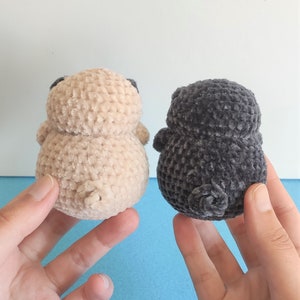 May include: Two crocheted plush toys shaped like pugs. One is beige and the other is gray.