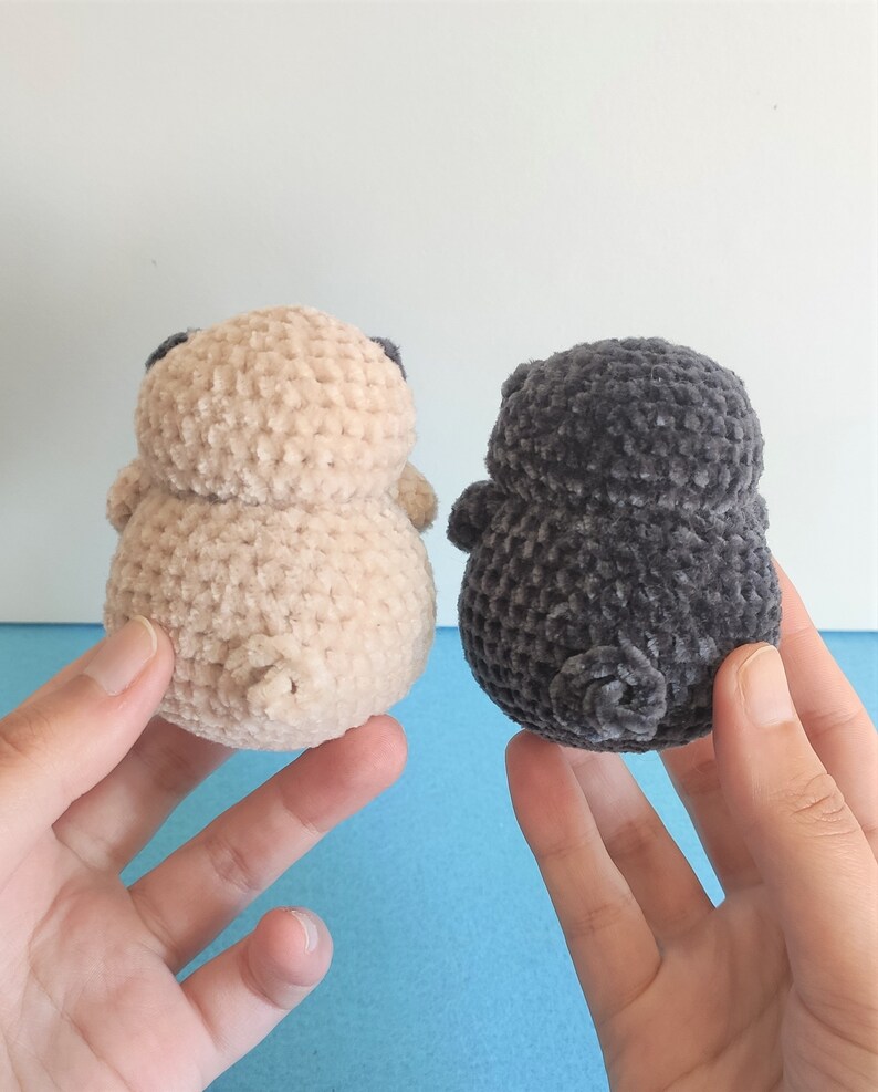 May include: Two crocheted plush toys shaped like pugs. One is beige and the other is gray.