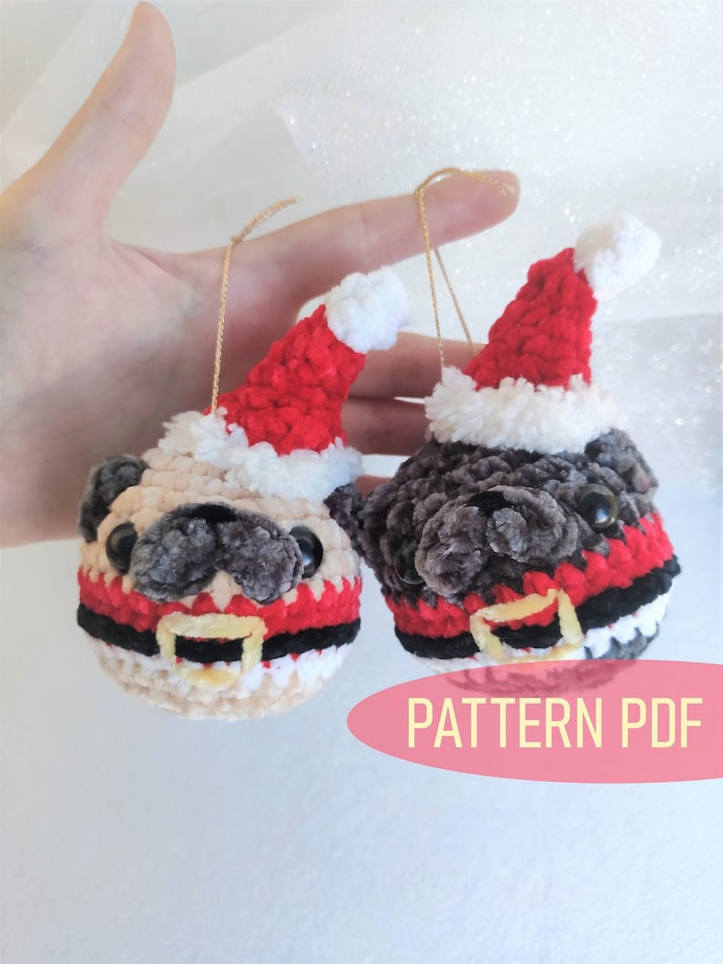 Pu&ograve; includere: Due ornamenti di pug in crochet che indossano cappelli di Babbo Natale e abiti rossi e bianchi. Gli ornamenti sono appesi a stringhe dorate. Il testo "PATTERN PDF" &egrave; visibile nell'immagine.