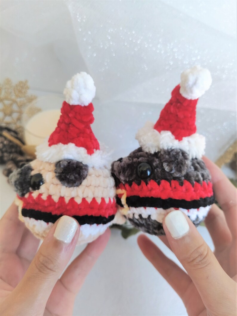 Pu&ograve; includere: Due giocattoli di peluche all'uncinetto a forma di carlino che indossano cappelli da Babbo Natale. I carlini indossano sciarpe a righe rosse e nere. Un carlino &egrave; beige e l'altro &egrave; grigio.
