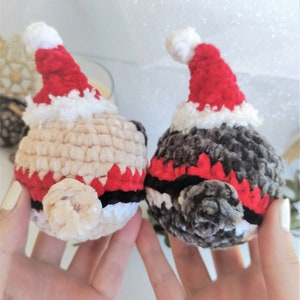 Pu&ograve; includere: Due giocattoli di peluche all'uncinetto con cappelli da Babbo Natale. Uno &egrave; beige con accenti rossi e neri, l'altro &egrave; grigio con accenti rossi e neri.