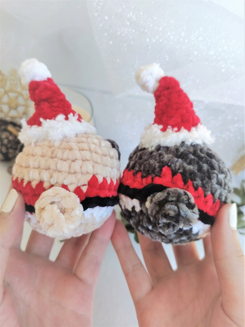 Pu&ograve; includere: Due giocattoli di peluche all'uncinetto con cappelli da Babbo Natale. Uno &egrave; beige con accenti rossi e neri, l'altro &egrave; grigio con accenti rossi e neri.