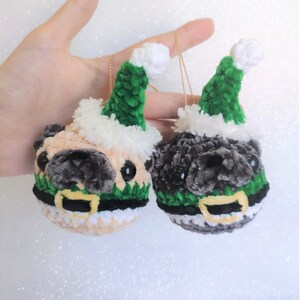 Pu&ograve; includere: Due ornamenti di pug all'uncinetto che indossano cappelli di Babbo Natale verdi con bordino bianco. Un pug &egrave; beige e l'altro &egrave; grigio.