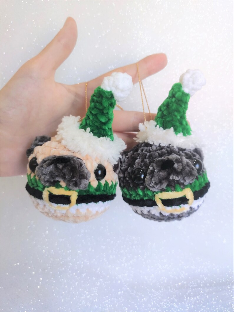 Pu&ograve; includere: Due ornamenti di pug all'uncinetto che indossano cappelli di Babbo Natale verdi con bordino bianco. Un pug &egrave; beige e l'altro &egrave; grigio.