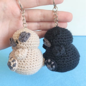May include: Two crocheted animal keychains, one beige and one black, with gray accents. The keychains are attached to silver key rings.