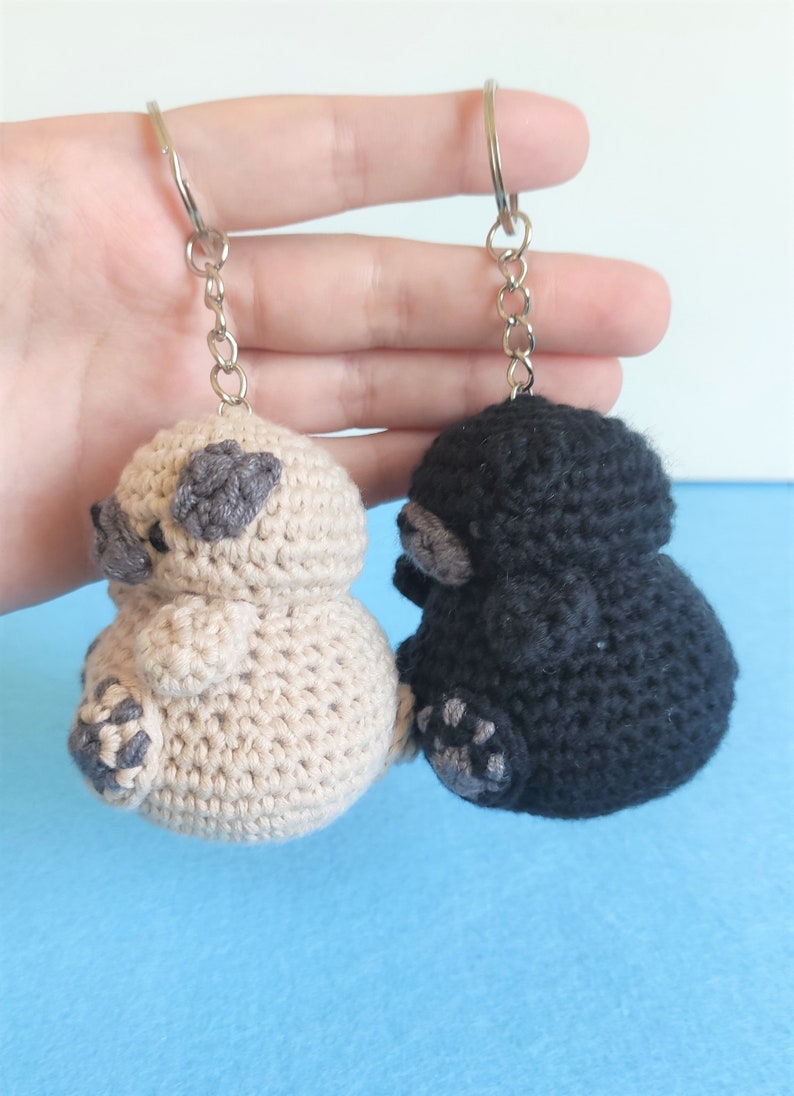 May include: Two crocheted animal keychains, one beige and one black, with gray accents. The keychains are attached to silver key rings.