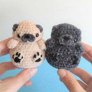 May include: Two crocheted plush toys, one beige and one gray, shaped like pugs. Both have black eyes and noses.