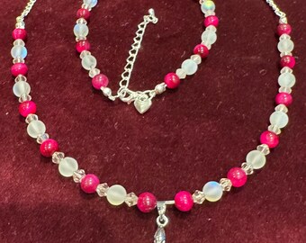 Puede incluir: Un conjunto de collar y pulsera de plata con cuentas rosas y blancas. El collar tiene un colgante de plata en forma de corazón con un diseño de mariposa.