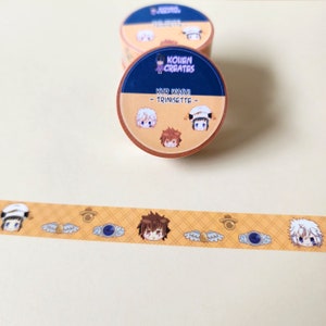 May include: A yellow and brown washi tape with a repeating pattern of cartoon characters, wings, and a blue eye. The tape is labeled "KHR WASHI - TRINISSETTE -" and "KOIEN CREATES".