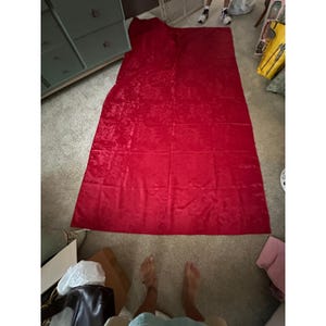 May include: A large, rectangular piece of red fabric featuring a subtle, tonal damask pattern with swirling floral motifs. The material has a slight sheen and is laid out flat, displaying a consistent deep red color across its entire surface area.