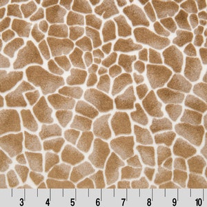 May include: Close-up of a fabric with a giraffe print. The pattern features irregular brown shapes separated by white spaces. The ruler at the bottom measures up to 12 inches.
