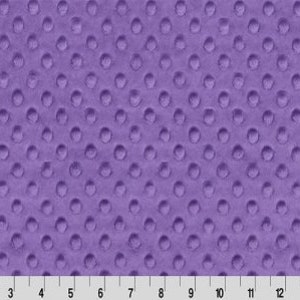 May include: Close-up of a textured, lavender fabric with a raised dot pattern. The fabric is evenly lit, showing the consistent texture. A ruler is at the bottom, with markings in inches.