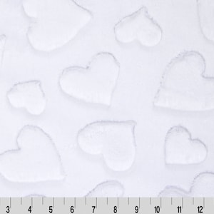 May include: White plush fabric with a repeating heart pattern. The hearts are raised and have a soft, textured appearance. A ruler is at the bottom of the image, showing measurements in inches.