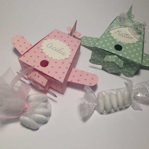 Può includere: Due piccole scatole portaconfetti a forma di aeroplano di carta, una rosa con pois bianchi e il nome "Cecilia" e una verde con cuori bianchi e il nome "Matteo".