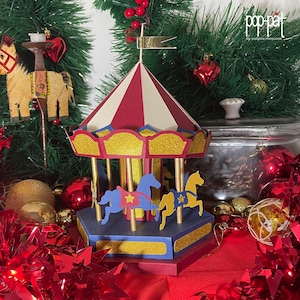 May include: A red, white, and blue carousel with gold trim and two horses. The carousel is decorated with glitter and has a red base. The carousel is surrounded by red and gold Christmas decorations.