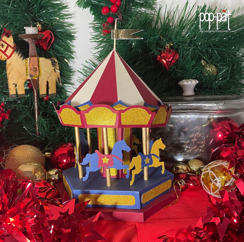 May include: A red, white, and blue carousel with gold trim and two horses. The carousel is decorated with glitter and has a red base. The carousel is surrounded by red and gold Christmas decorations.