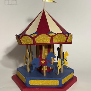 Peut inclure: Un carrousel en papier rouge, blanc et bleu avec des accents de paillettes dorées et un drapeau jaune sur le dessus. Le carrousel a six chevaux, dont deux sont jaunes, deux sont bleus et deux sont rouges.