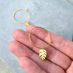 May include: Gold hoop earrings with a small, gold, leaf-shaped charm hanging from each hoop.