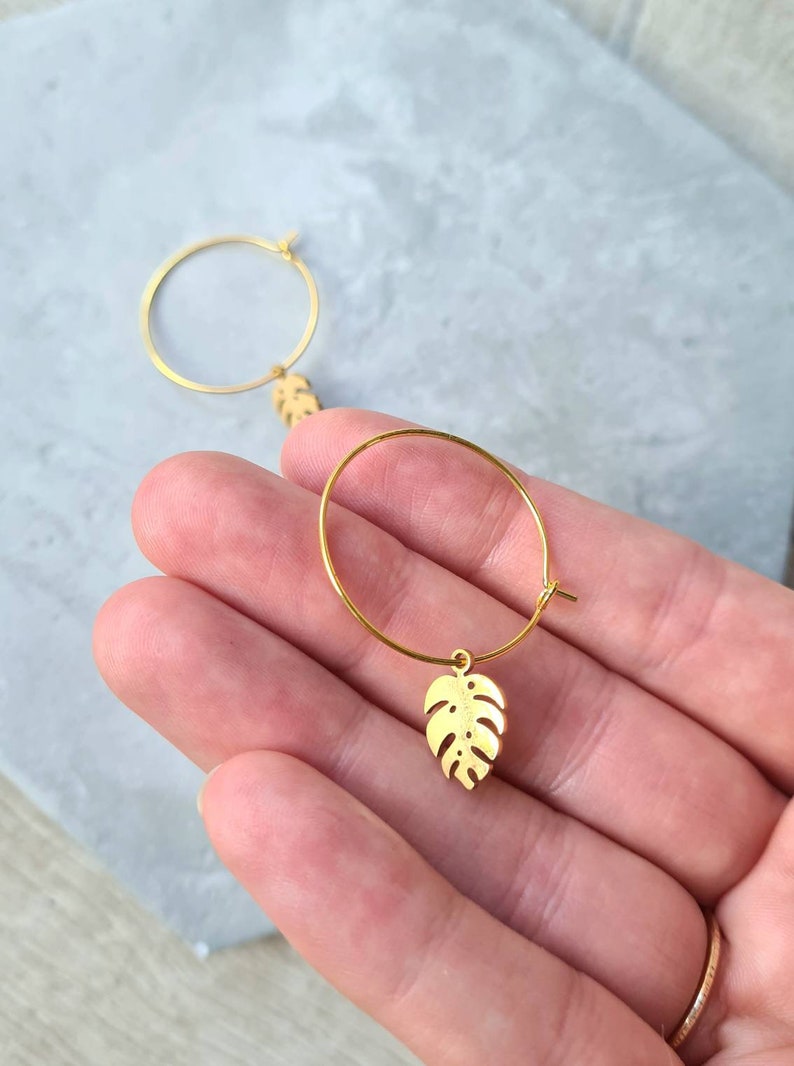 May include: Gold hoop earrings with a small, gold, leaf-shaped charm hanging from each hoop.