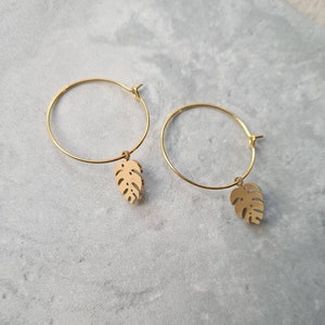 May include: Gold hoop earrings with a small, gold, cutout leaf charm hanging from each hoop.