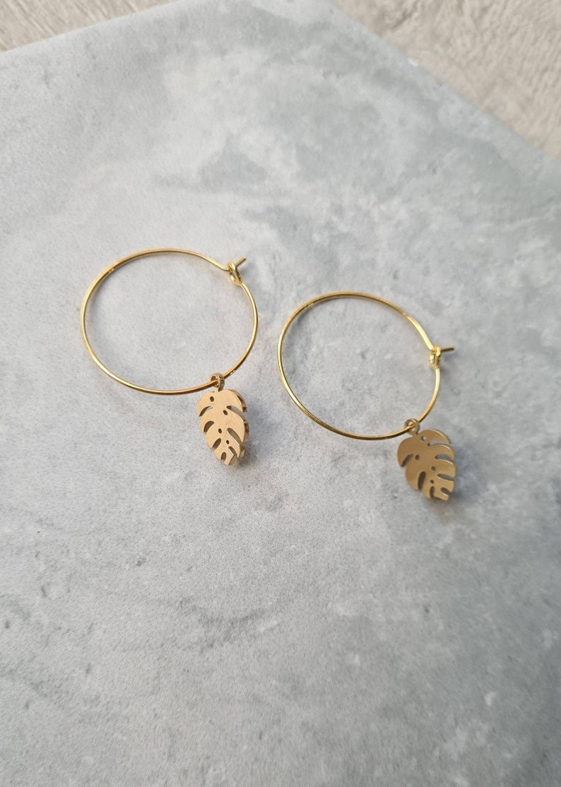 May include: Gold hoop earrings with a small, gold, cutout leaf charm hanging from each hoop.