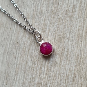May include: A silver chain necklace with a small, round, red gemstone pendant.