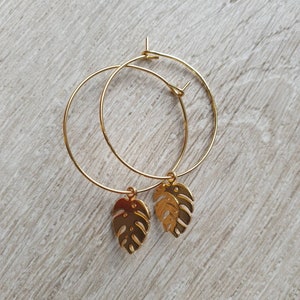 May include: Gold hoop earrings with a gold monstera leaf charm hanging from each hoop.