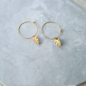 May include: A pair of gold hoop earrings with a small gold leaf charm hanging from each hoop.