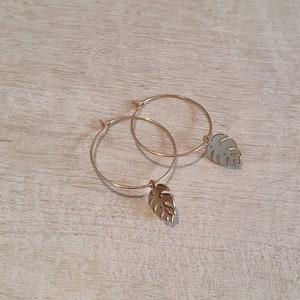 May include: Gold hoop earrings with a small, gold, leaf-shaped charm hanging from each hoop.