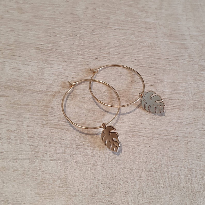 May include: Gold hoop earrings with a small, gold, leaf-shaped charm hanging from each hoop.
