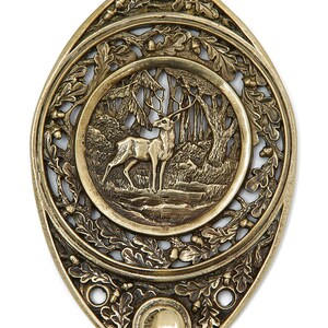 May include: A brass coat hook in the shape of a teardrop with an ornate design featuring a deer in a forest scene. The hook is attached to the bottom of the teardrop.