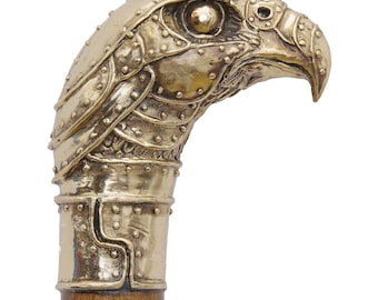 May include: A brass cane handle shaped like an eagle head with a riveted metal plate design. The eagle features a sharp beak and detailed eye. The handle is attached to a wooden shaft. The text ARTBRASSFORYOU is visible at the bottom right.