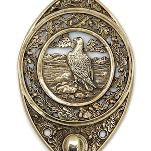 May include: A gold-toned metal hook with an ornate design featuring an eagle perched on a rock in a mountainous landscape. The hook is surrounded by a decorative border of oak leaves and acorns.