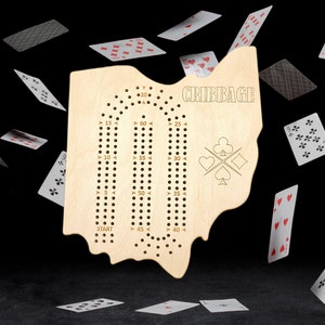 May include: A wooden cribbage board shaped like the state of Ohio. The board has a scoring track with numbers from 0 to 120. The word "CRIBBAGE" is printed at the top of the board.