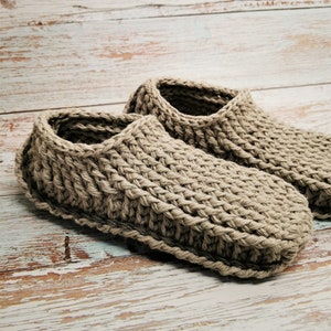 May include: A pair of beige crocheted slippers on a whitewashed wooden surface.