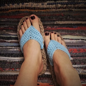 May include: A pair of blue crocheted sandals with brown leather straps. The sandals are worn on a person's feet.