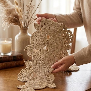 Könnte beinhalten: Ein beigefarbener Häkel-Tischläufer mit einer Reihe von miteinander verbundenen kreisförmigen und blattförmigen Motiven. Das Textil ist aus feinem Garn mit einem gleichmäßigen, festen Stichmuster gefertigt, das eine strukturierte Anordnung ergibt.