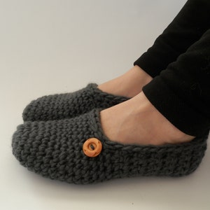 May include: Gray knitted slippers with a wooden button on the top. The slippers are worn on a person's feet.
