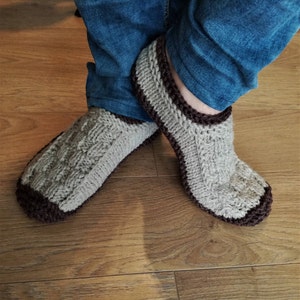 May include: A pair of knitted slippers with a brown trim. The slippers are made of a light gray yarn and have a cable knit pattern.