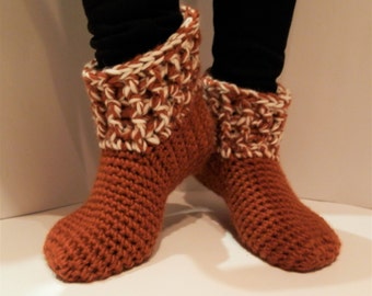 Può includere: Stivali da camera in crochet di colore marrone e bianco. Gli stivali hanno un polsino in crochet bianco e un corpo in crochet marrone.
