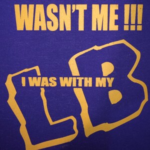 May include: Purple t-shirt with gold lettering that reads "Wasn't me!!! I was with my LB".
