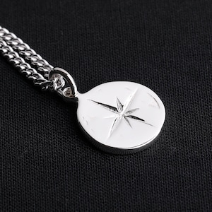 May include: A silver chain necklace with a round pendant featuring a starburst design.