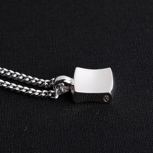 May include: A silver chain necklace with a silver pendant. The pendant is a rectangular shape with rounded edges. The pendant has a smooth, polished surface.