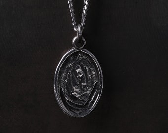 May include: A silver chain necklace with an oval pendant featuring a detailed design. The pendant has a textured surface and appears to be made of metal.