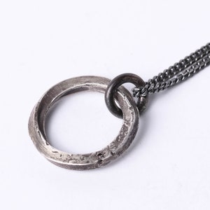 Könnte beinhalten: Eine silberne Kettenkette mit einem texturierten silbernen Ringanhänger. Der Ring ist doppelschichtig und hat eine leicht oxidierte Oberfläche.