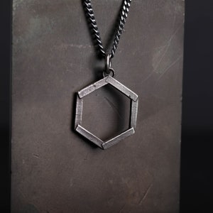 May include: A silver chain necklace with a hexagonal pendant. The pendant is made of metal and has a geometric design.