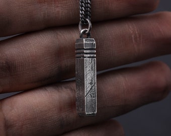 May include: A silver chain necklace with a rectangular pendant. The pendant has a textured surface and a slightly rounded top and bottom.