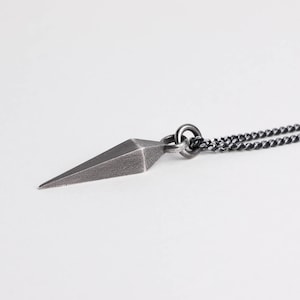 Könnte beinhalten: Eine silberne Halskette mit einem geometrischen Anhänger in Form einer scharfen Spitze. Die Kette ist eine schwarze oxidierte Panzerkette.