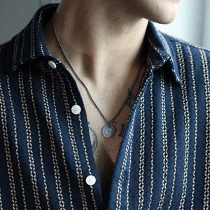 May include: A person wearing a dark blue and white striped shirt with a silver chain necklace and a round pendant.