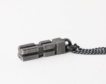 May include: A silver chain necklace with a geometric pendant. The pendant is made of stacked rectangular shapes and has a textured surface.